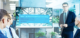 Männer halten ein Meeting in einem Konferenzraum. Einer von ihnen hält eine sellify Präsentation an einem Bildschirm.
