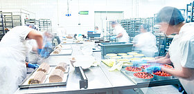 Das Bild zeigt Menschen in eine Großküche bei der Fertigung verschiedener Kuchen